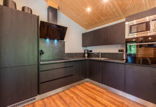 Moderna cucina nera nel lodge Hackfort al parco vacanze De Wiltzangh nei Paesi Bassi, con pavimento in legno.