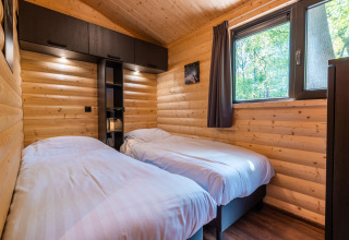 Slaapkamer met twee eenpersoonsbedden in Hackfort lodge in vakantiepark De Wiltzangh, Nederland, houten muren.