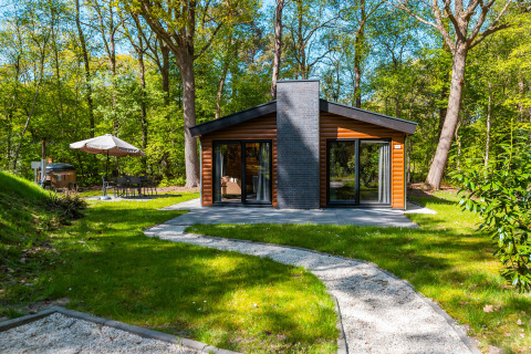 Lodge Hackfort op vakantiepark De Wiltzangh in Nederland, omringd door bos en een terras met zithoek.