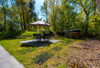 Zona exterior con mesa, sillas y sombrilla junto a un jacuzzi en lodge Hackfort, De Wiltzangh, Holanda.
