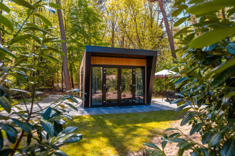 Moderna lodge Just Nature con ampie porte in vetro, immersa nel verde lussureggiante e alberi alti del bosco.