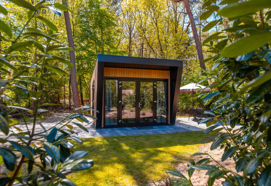Moderna lodge Just Nature con ampie porte in vetro, immersa nel verde lussureggiante e alberi alti del bosco.