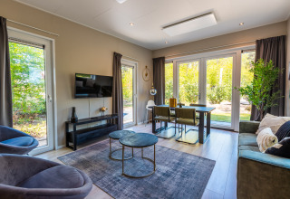 Moderne og lys stue på lodge Just Nature i Holiday park De Wiltzangh, med store vinduer og stilfuldt interiør.