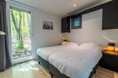 Slaapkamer in de Just Nature-lodge op vakantiepark De Wiltzangh, met boszicht door glazen deur.