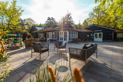 Sonnige Terrasse mit Lounge-Möbeln vor der Just Nature Lodge im Ferienpark De Wiltzangh, Niederlande.