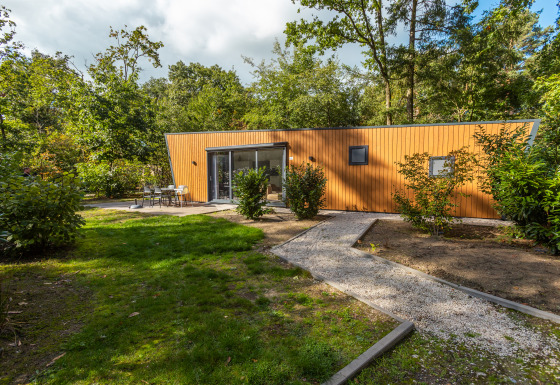 Een modern houten lodge bij Just Nature Hot tub, omgeven door groene bomen en een rustige tuin.