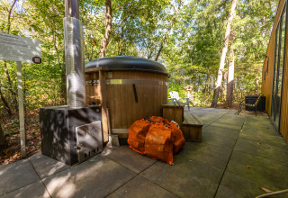 Houten buitenbad met kachel bij lodge Just Nature in vakantiepark De Wiltzangh, Nederland, omringd door bos.