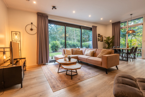 Modernes Wohnzimmer in der Just Nature Lodge, De Wiltzangh Ferienpark, mit Waldblick und großen Fenstern.