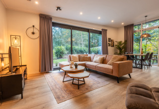 Moderne woonkamer in lodge Just Nature, De Wiltzangh, met grote ramen en uitzicht op de natuur.