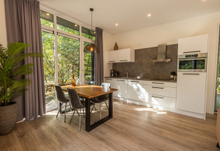 Modern kitchen and dining area with large windows and garden view in Just Nature lodge, De Wiltzangh, Netherlands.