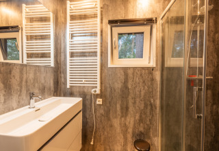 Salle de bains moderne avec miroir, lavabo, chauffe-serviettes et douche à Just Nature, De Wiltzangh, Pays-Bas.