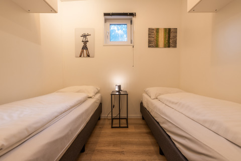 Room with two single beds, a nightstand and wall art in Just Nature lodge at De Wiltzangh, Netherlands.