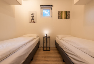 Habitación con dos camas individuales, mesita y arte en la pared en la cabaña Just Nature, De Wiltzangh, Países Bajos.