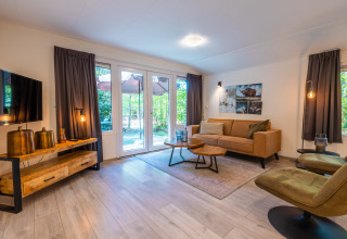 Salon moderne au lodge Stuga dans le parc De Wiltzangh, Pays-Bas, avec canapé, TV et vue sur la nature.