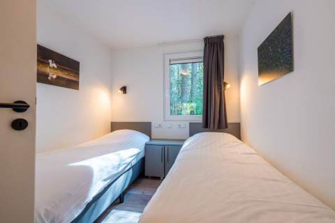 Camas individuales en habitación luminosa con ventana y vista al bosque, Stuga en De Wiltzangh, Países Bajos.