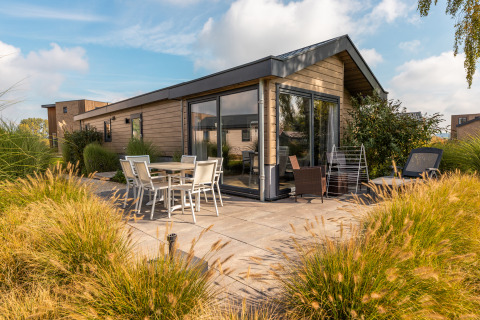 Buitenterras bij Velthorst-lodge met eettafel, stoelen en modern houten huis omringd door siergrassen.
