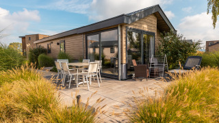 Udendørs terrasse ved Velthorst-lodge med spisebord, stole og moderne træhus omgivet af vilde græsser.