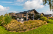 Moderne Velthorst lodge op vakantiepark Aan de Maas in Nederland, omgeven door tuin en groene beplanting.