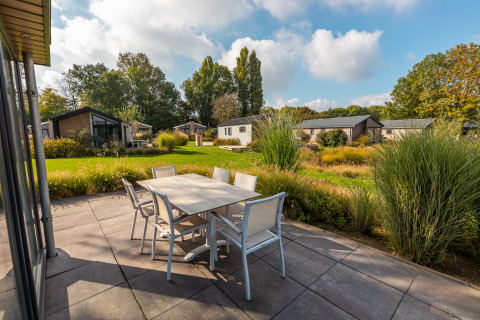 Terras met eettafel bij lodge Velthorst in vakantiepark Aan de Maas, Nederland, omgeven door veel groen.