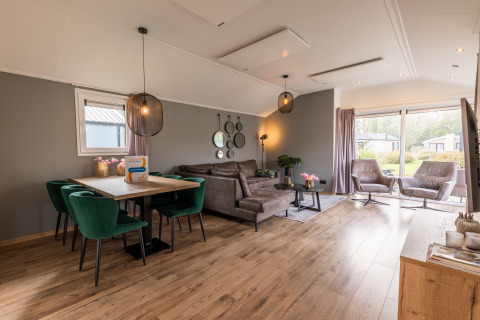 Modern living and dining area in the Velthorst lodge at Holiday park Aan de Maas, featuring large windows and cozy furniture.