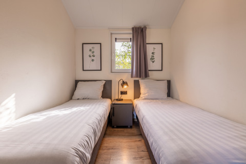 Due letti singoli nel lodge Velthorst, Holiday park Aan de Maas, Paesi Bassi, con finestra e arte botanica.