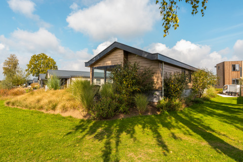 Velthorst lodge at Holiday park Aan de Maas in the Netherlands, surrounded by green plants and a blue sky.