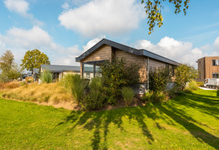 Velthorst-lodge bij vakantiepark Aan de Maas in Nederland, omgeven door groene planten en blauwe lucht.