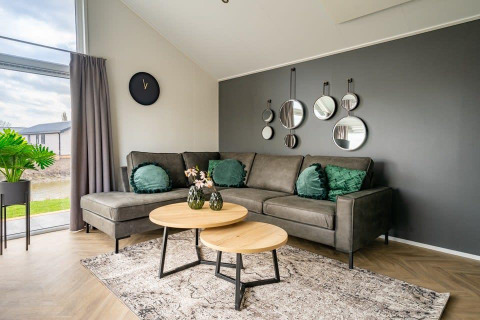 Modernes Wohnzimmer im Tiny House Velthorst im Holidaypark Aan de Maas, mit grauem Sofa und grünen Kissen.