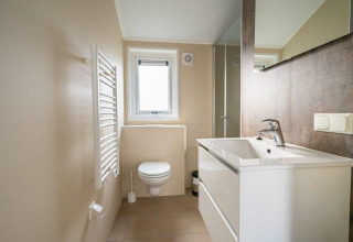 Bagno moderno nella tiny house ‘Velthorst’ al Holiday park Aan de Maas, Paesi Bassi, con lavabo e finestra.