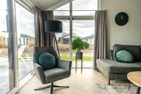 Moderne zithoek in tiny house 'Velthorst' met stoel en grote ramen in vakantiepark Aan de Maas.