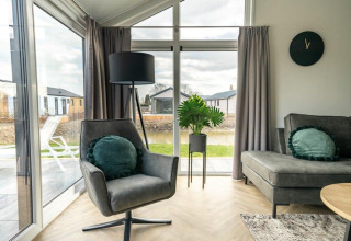 Salon contemporain dans la tiny house « Velthorst » avec fauteuil et grandes fenêtres au Holiday park Aan de Maas.