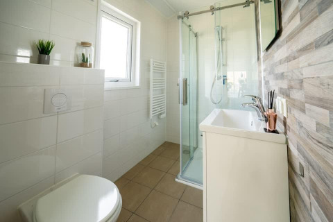 Modern bathroom in a tiny house at Holiday park Aan de Maas, Netherlands, featuring glass shower and plants.