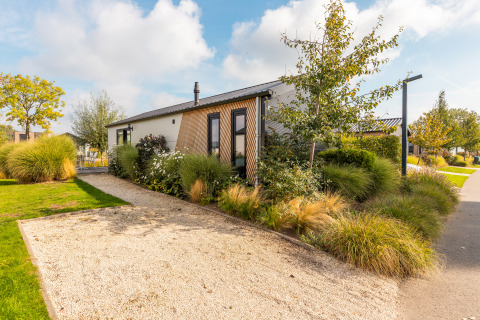 Moderno lodge Berkel circondato da verde e piante ornamentali, con vialetto di ghiaia al sole.