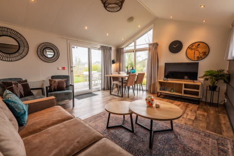 Wohnzimmer im Lodge Berkel im Ferienpark Aan de Maas, Niederlande, mit moderner Einrichtung und Panoramafenster.