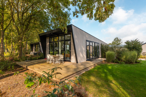 Moderne Lodge mit großen Fenstern und Holzterrasse im Grünen, ausgestattet mit Essbereich im Freien.