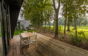 Houten terras met tafel en stoelen bij lodge Just Nature, Holiday park Aan de Maas, omringd door natuur.