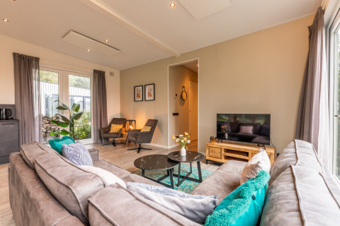 Soggiorno moderno nella lodge 'Just Nature' al Holiday park Aan de Maas, Paesi Bassi, con divano e TV.