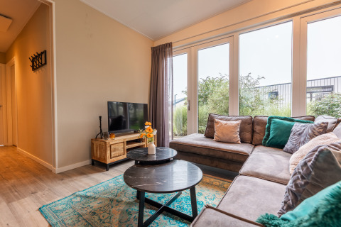 Woonkamer in lodge ‘Just Nature’ bij Holiday park Aan de Maas, met zetel, tv en grote raampartijen.