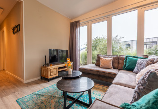 Woonkamer in lodge ‘Just Nature’ bij Holiday park Aan de Maas, met zetel, tv en grote raampartijen.