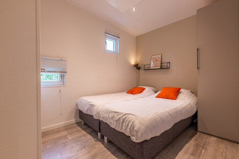 Chambre moderne dans la lodge Just Nature au Holiday park Aan de Maas aux Pays-Bas, avec lits jumeaux et coussins orange.