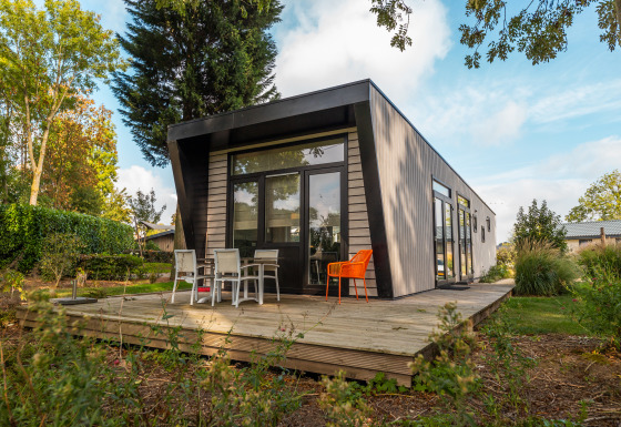 Moderne lodge genaamd Just Nature, omgeven door groen, terras met stoelen, zonnige dag.