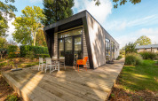 Modern lodge named Just Nature at Holiday park Aan de Maas, Netherlands, with a wooden deck and garden setting.