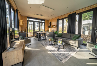 Moderne lodge-stue ved Holiday park Aan de Maas i Holland med store vinduer og stilfuld indretning.