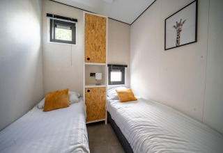 Kamer met twee eenpersoonsbedden, gele kussens, minimalistisch interieur en ramen in Just Nature lodge bij Holiday park Aan de Maas.