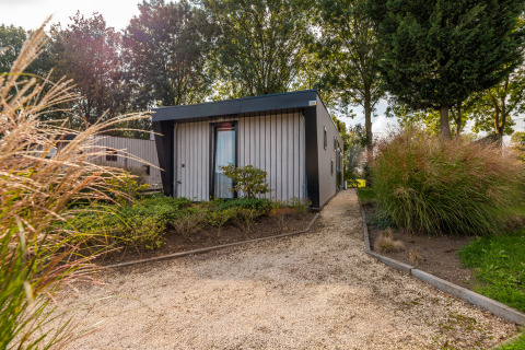 Eingang zur Just Nature Lodge im Ferienpark Aan de Maas, Niederlande, umgeben von Bäumen und Sträuchern.