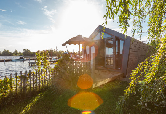 Solrig udsigt over vandet fra Tiny House Havenzicht, med træterrasse og haver med grønne planter.