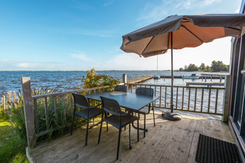 Outdoor lakeside terrace with table, four chairs, and parasol at Tiny House Havenzicht, De Wiedense Meren.
