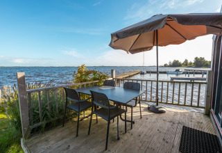 Outdoor lakeside terrace with table, four chairs, and parasol at Tiny House Havenzicht, De Wiedense Meren.