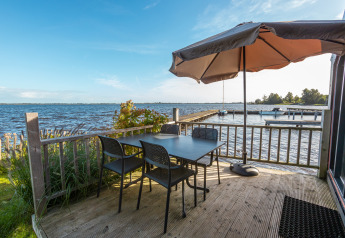 Buitenterras aan het water met tafel, vier stoelen en een parasol bij Tiny House Havenzicht, De Wiedense Meren.