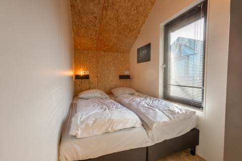Bedroom in Tiny House «Havenzicht» at Holiday park De Wiedense Meren featuring twin beds and a window.